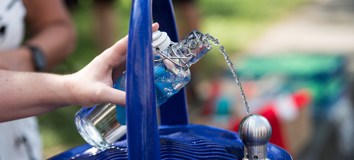 An einem Trinkwasserbrunnen wird eine Flasche mit Wasser gefüllt.