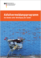 Vor einer Ziegelsteinmauer von der blaue Farbe abblättert, steht ein verrosteter Einkaufswagen.  Dieser ist bis zum Rand gefüllt mit zerknüllten Verpackungsresten aus Pappe und Plastik.