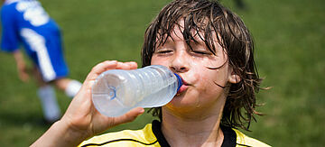 Durstiger junger Fußballspieler trinkt Wasser am Rande des Spielfeldes.