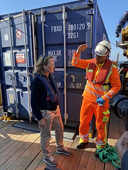 Steffi Lemke spricht mit einem freiwilligen Helfer vor einem blauen Schiffscontainer.