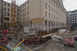 Blick auf eine Baustelle mit Kran. Im Zentrum eine größtenteils unterirdisch angelegte Raumkonstruktion im Rohbauzustand. Im Hintergrund eine nach unten in diesen Raum verlaufende Zufahrtsstraße