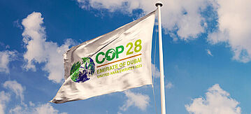 Flagge mit COP28-Logo vor blauem Himmel