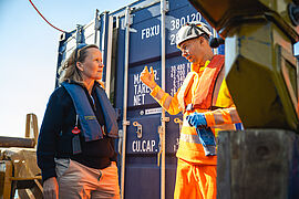 Steffi Lemke spricht mit einem freiwilligen Helfer vor einem blauen Schiffscontainer.