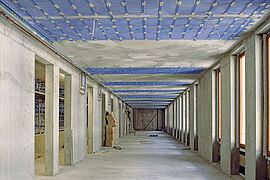 Blick in einen weiten Flur im Rohbauzustand, an der Decke sind in Abständen blaue Bahnen für das Heizsystem verklebt.