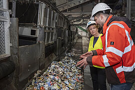 Ministerin Steffi Lemke und Christian Hündgen stehen am Sortierungsband mit Müll.