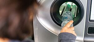 Eine Frau legt eine leere Plastikflasche in einen Pfandautomaten