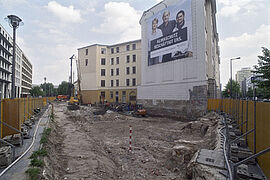 Eine von Bauzaun umgebene Baustelle mit diversen Baustellenfahrzeugen auf der die Aushubarbeiten aufgenommen worden sind.