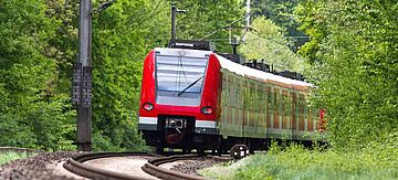 Eine rote Regionalbahn fährt durch einen Wald