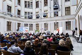 Blick in den Saal mit Publikum im Veranstaltungshof des BMUV, während Claudia Roth eine Rede hält.